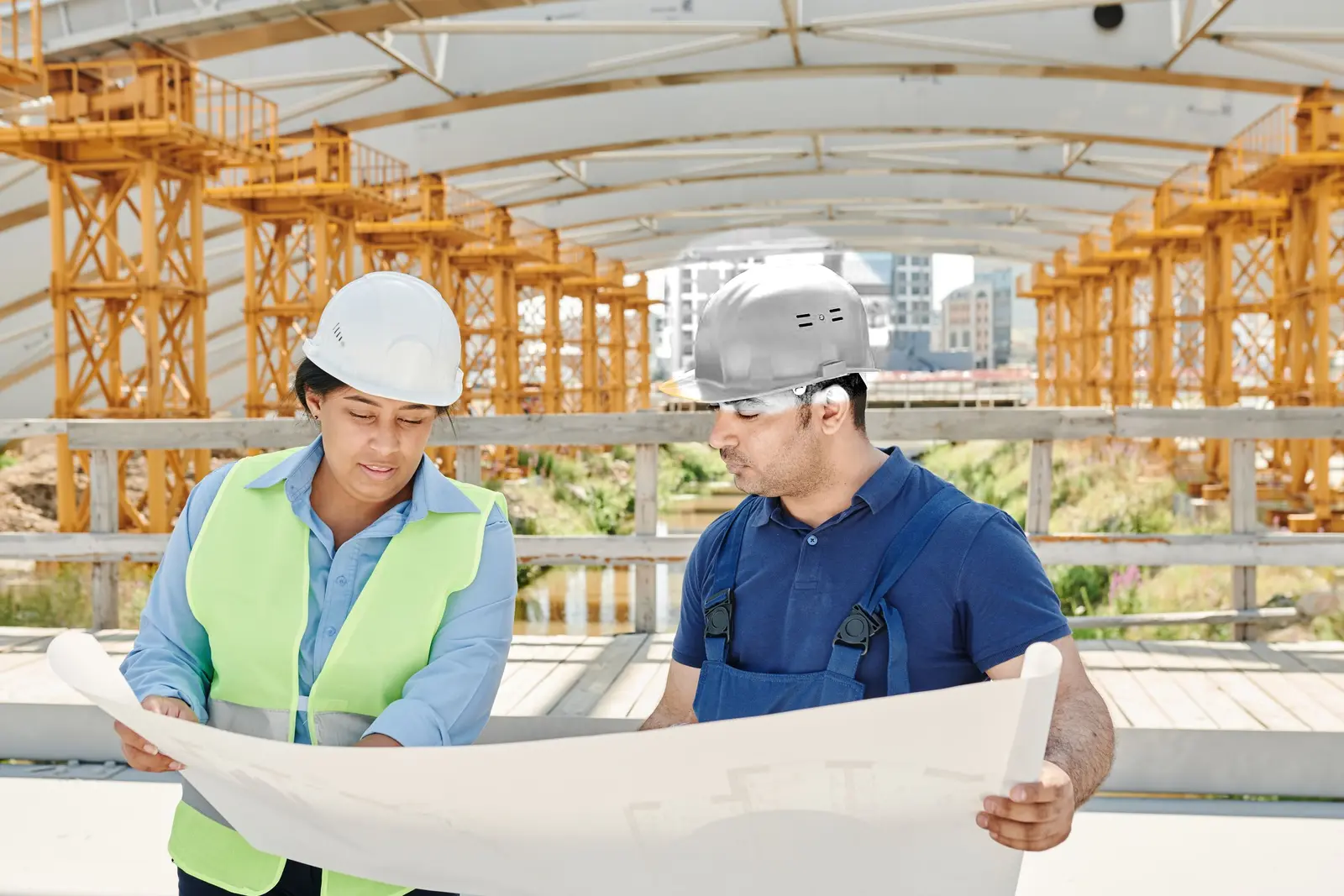 A woman and man in white hard hats reviewing project plans
